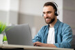 © Prostock-studio - Smiling male employee wearing wireless headphones working on computer in modern office