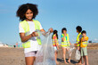 Happy teen curly african american girl puts bottle in bag, different kids volunteers in vests collect garbage