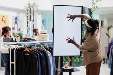 Man touching interactive whiteboard to view shoe advertisement in clothing store. African american customer interacting with white blanck digital screen while shopping in mall