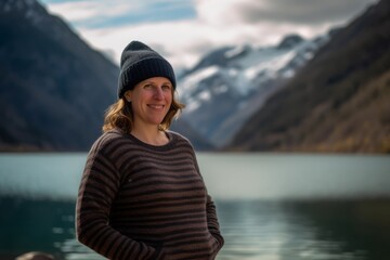 Wall Mural - Young woman in a sweater and hat on the background of a mountain lake