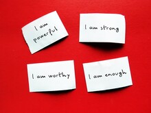 Four Paper Pieces On Red Background With Handwritten Text I AM STRONG, I AM WORTHY, I AM ENOUGH, I AM POWERFUL, Positive Self Talk Affirmations To Boost Self Confidence