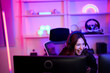 © MergeIdea - Asian e-sport woman laugh with fun emotional because of happy playing game when she live and share monitor screen on her channel and social media in entertainment gamer room with neon light
