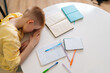 © dikushin - High-angle view of tired student pupil boy lying on desk filled with books training material. Frustrated little child boy sleeping while doing homework with head on table. Fatigue, education concept