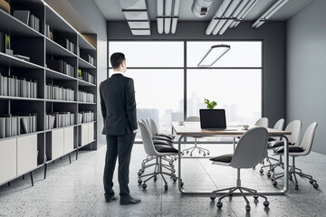 Poster - Work process with businessman back view in modern conference room interior design with wooden table and chairs on steel legs, concrete floor, huge bookshelf and city view background from big window