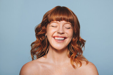 Happy woman with ginger hair and flawless skin smiling with her eyes closed