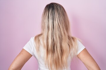 Poster - Young blonde woman standing over pink background standing backwards looking away with arms on body