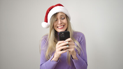 Poster - Young blonde woman wearing christmas hat using smartphone over isolated white background