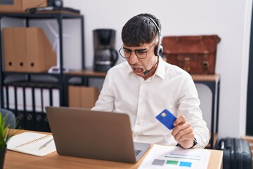 Wall Mural - Young hispanic man working using computer laptop holding credit card angry and mad screaming frustrated and furious, shouting with anger. rage and aggressive concept.