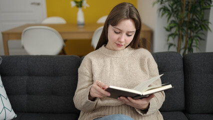 Sticker - Young blonde woman reading book sitting on sofa at home