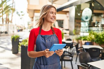 Young hispanic woman waitress smiling confident using touchpad at coffee shop terrace