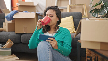 Sticker - Young beautiful hispanic woman watching video on smartphone drinking coffee at new home