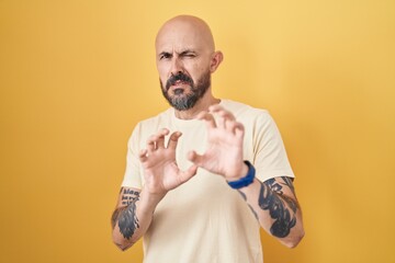 Poster - Hispanic man with tattoos standing over yellow background disgusted expression, displeased and fearful doing disgust face because aversion reaction.