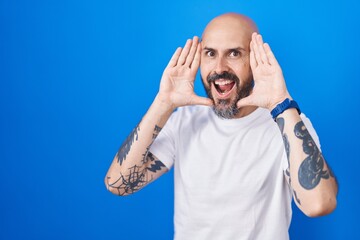 Sticker - Hispanic man with tattoos standing over blue background smiling cheerful playing peek a boo with hands showing face. surprised and exited