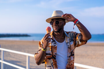 Wall Mural - Black ethnic man enjoy summer vacation on the beach eating an ice cream having fun