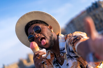 Wall Mural - Portrait of a black ethnic man enjoying summer vacation at the beach eating an ice cream taking a selfie