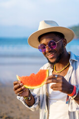 Wall Mural - black ethnic man enjoy summer vacation at the beach eating a watermelon smiling