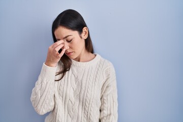 Young brunette woman standing over blue background tired rubbing nose and eyes feeling fatigue and headache. stress and frustration concept.