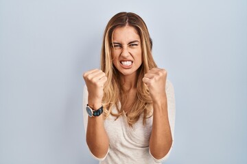 Canvas Print - Young blonde woman standing over isolated background angry and mad raising fists frustrated and furious while shouting with anger. rage and aggressive concept.