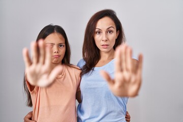 Wall Mural - Young mother and daughter standing over white background doing stop sing with palm of the hand. warning expression with negative and serious gesture on the face.