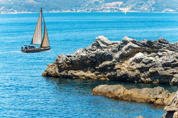 Wall Mural - White sailing boat in the Mediterranean sea and rocky coast with cliffs in the Gulf of La Spezia, Liguria, Italy, Europe.