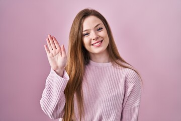 Poster - Young caucasian woman standing over pink background waiving saying hello happy and smiling, friendly welcome gesture