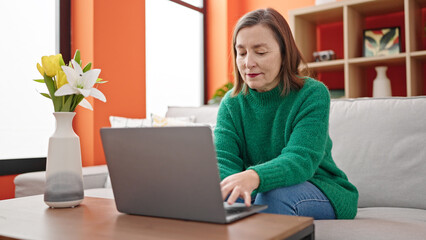 Sticker - Mature hispanic woman with grey hair using laptop sitting on sofa at home