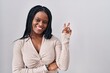 © Krakenimages.com - African woman with braids standing over white background smiling with happy face winking at the camera doing victory sign with fingers. number two.