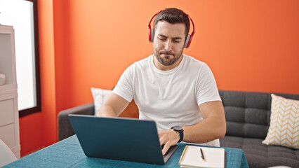 Sticker - Young hispanic man listening to music sitting on table at dinning room