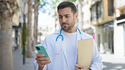 Poster - Young hispanic man doctor holding medical report using smartphone at street