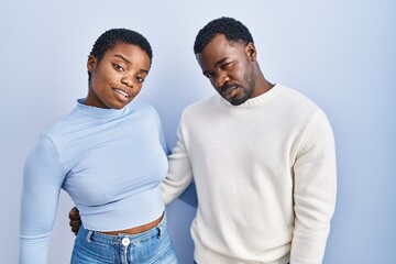 Poster - Young african american couple standing over blue background looking sleepy and tired, exhausted for fatigue and hangover, lazy eyes in the morning.