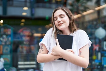 Sticker - Young woman smiling confident hugging book at street