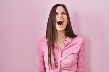 Sticker - Young hispanic woman standing over pink background angry and mad screaming frustrated and furious, shouting with anger. rage and aggressive concept.