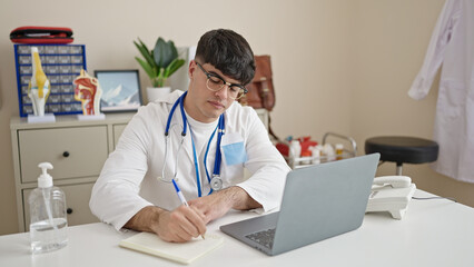 Canvas Print - Young hispanic man doctor using laptop writing notes at clinic