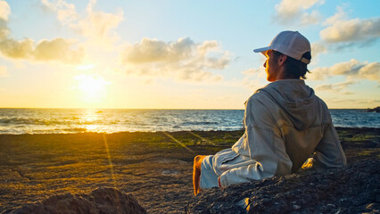 Wall Mural - Man on a beach is looking distance during beautiful summer sunset. Human looks to the sun over horizon in the morning while sunrise. Happy person contemplates the beauty of nature. Freedom concept.