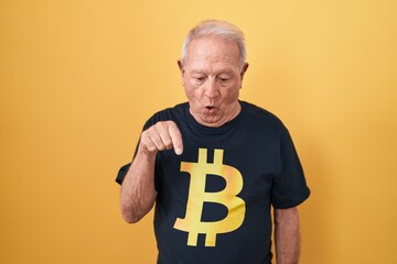 Poster - Senior man with grey hair wearing bitcoin t shirt pointing down with fingers showing advertisement, surprised face and open mouth