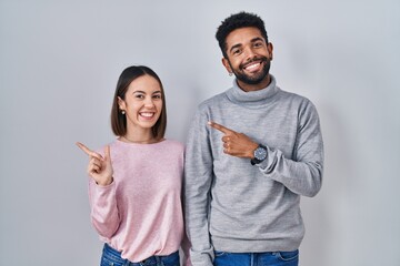 Canvas Print - Young hispanic couple standing together cheerful with a smile on face pointing with hand and finger up to the side with happy and natural expression