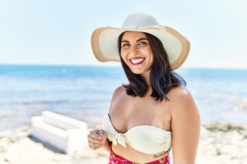 Canvas Print - Young beautiful hispanic woman tourist smiling confident wearing bikini and summer hat at seaside