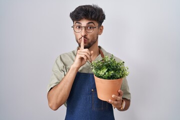 Sticker - Arab man with beard holding green plant pot asking to be quiet with finger on lips. silence and secret concept.