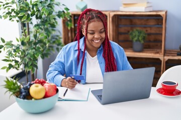 Sticker - African american woman using laptop and holding credit card at home