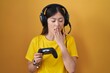 Chinese young woman playing video game holding controller bored yawning tired covering mouth with hand. restless and sleepiness.
