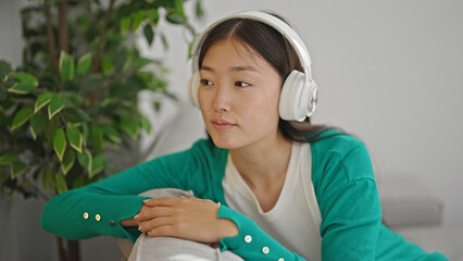 Wall Mural - Young chinese woman listening to music sitting on sofa at home