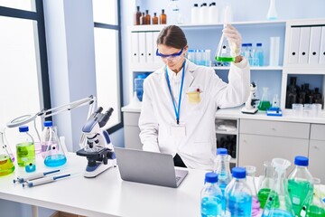 Wall Mural - Young caucasian woman scientist holding test tube using laptop at laboratory