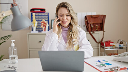 Sticker - Young blonde woman doctor using laptop talking on smartphone at clinic