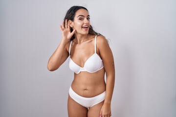 Canvas Print - Young hispanic woman wearing white lingerie smiling with hand over ear listening an hearing to rumor or gossip. deafness concept.