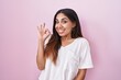 © Krakenimages.com - Young arab woman standing over pink background smiling positive doing ok sign with hand and fingers. successful expression.