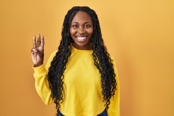 Poster - African woman standing over yellow background showing and pointing up with fingers number three while smiling confident and happy.