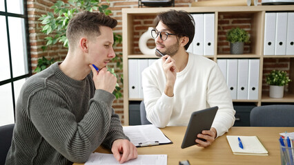 Two men business partners using touchpad working at office