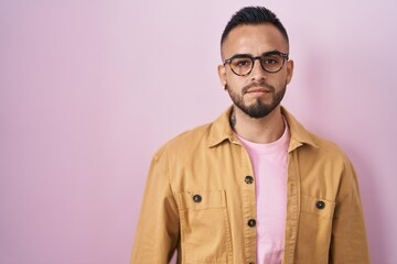 Sticker - Young hispanic man standing over pink background relaxed with serious expression on face. simple and natural looking at the camera.