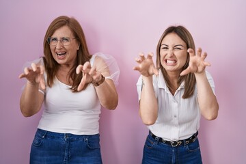 Canvas Print - Hispanic mother and daughter wearing casual white t shirt over pink background smiling funny doing claw gesture as cat, aggressive and sexy expression