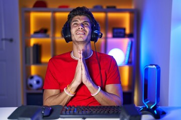 Canvas Print - Young hispanic man playing video games begging and praying with hands together with hope expression on face very emotional and worried. begging.